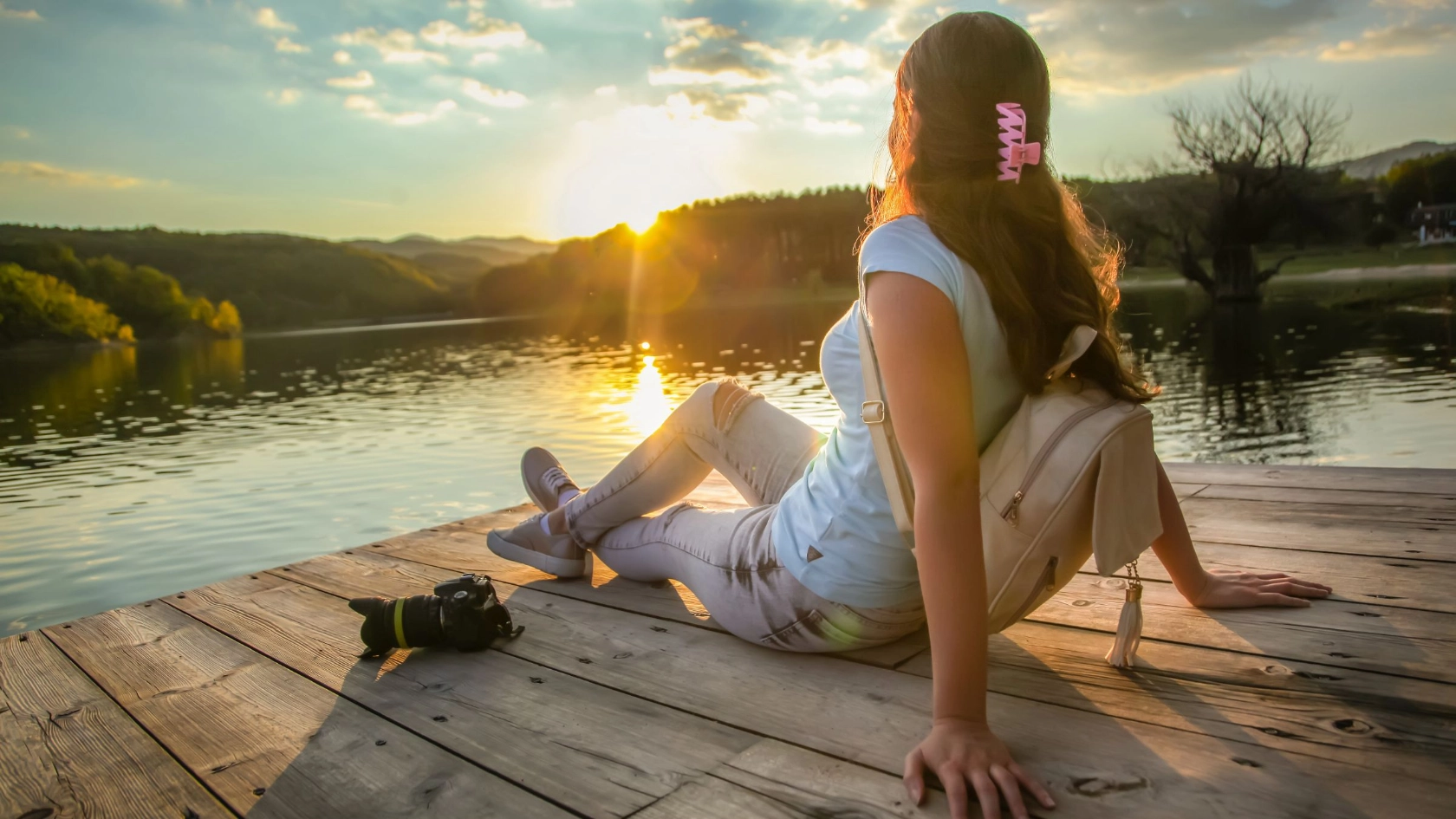 Junge Frau sitzt auf dem Steg und genießt den Sonnenuntergang