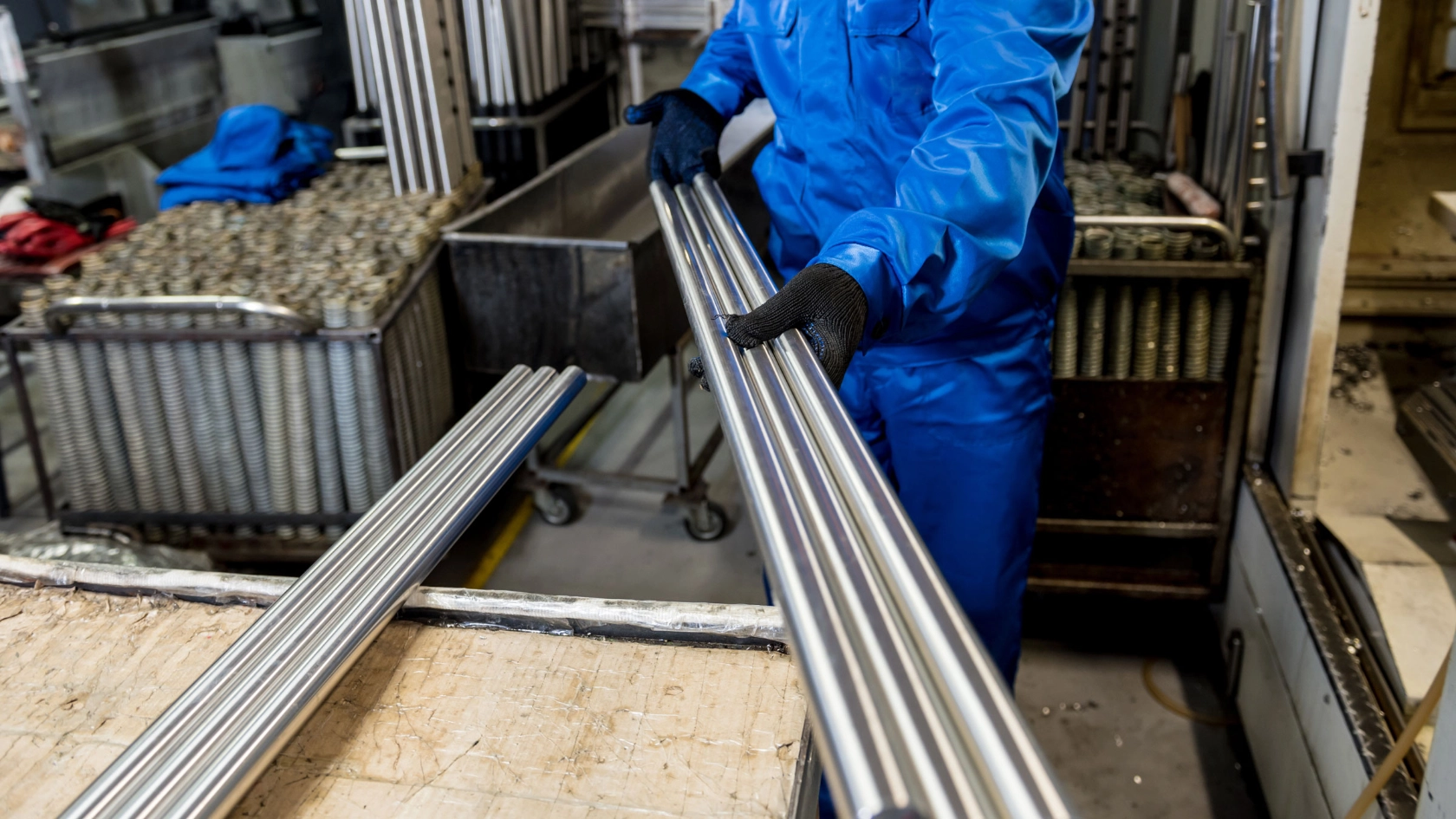 Ein Beschäftigter in einer Werkshalle hält Metallrohre in den Händen