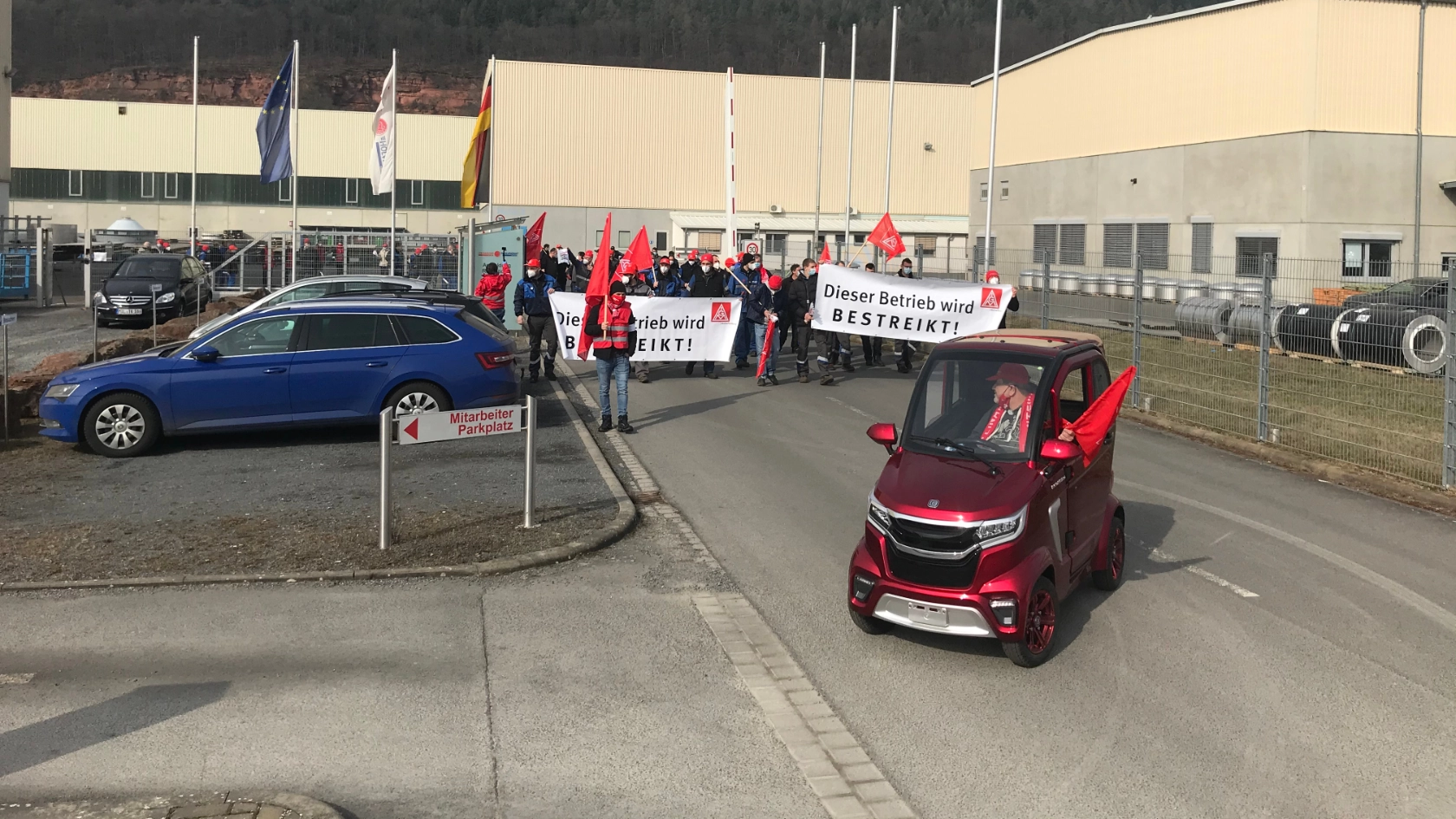 Ein kleines rotes Elektrofahrzeug führt eine Menge Warnstreikende Beschäftgite bei Ziemann Holvrieka in Bürgstadt an.