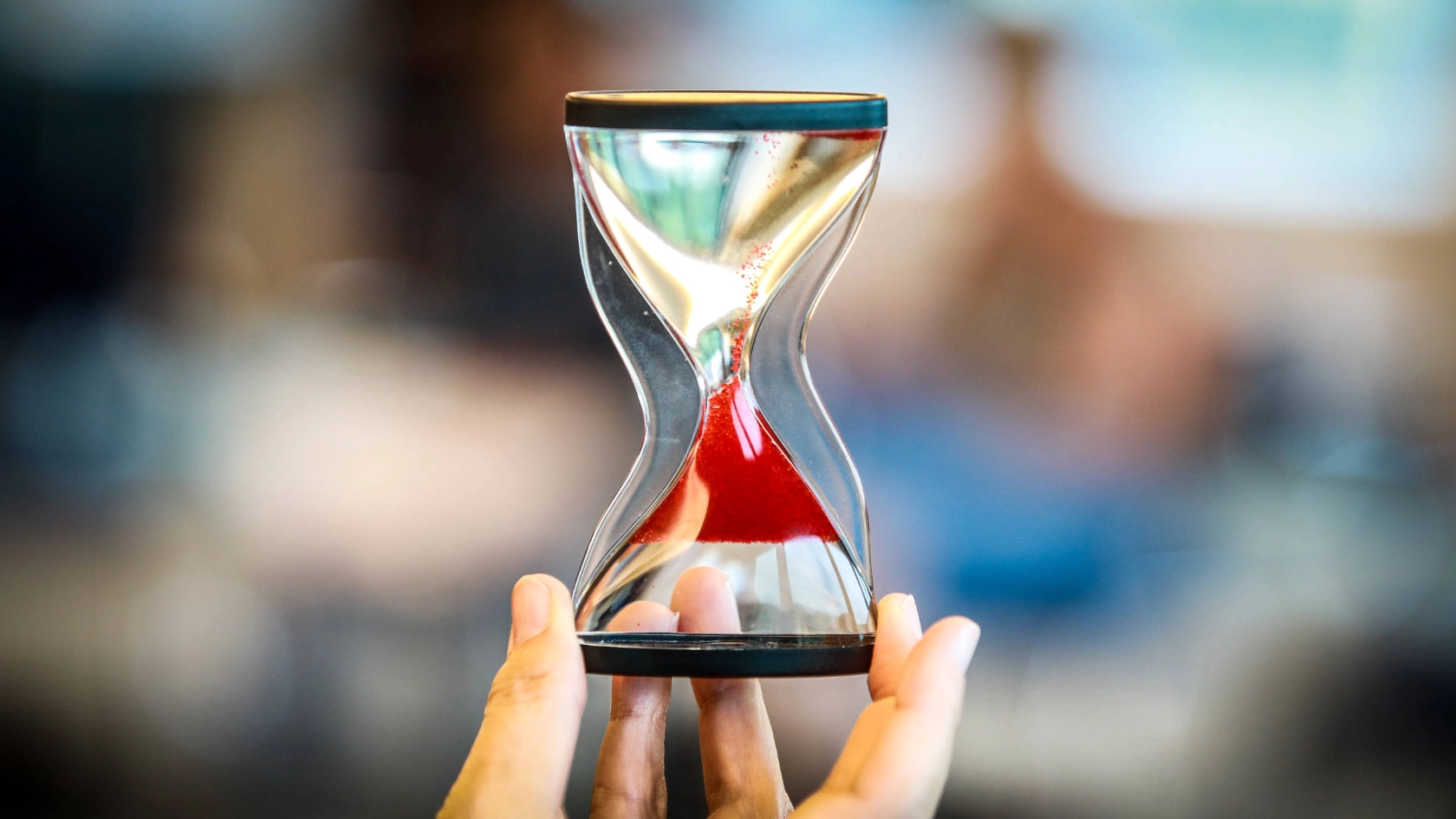 Eine Sanduhr, durch die roter Sand rinnt.