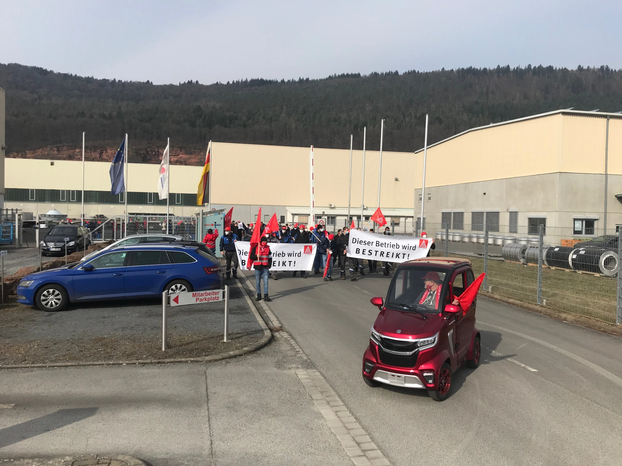 Ein kleines rotes Elektrofahrzeug führt eine Menge Warnstreikende Beschäftgite bei Ziemann Holvrieka in Bürgstadt an.