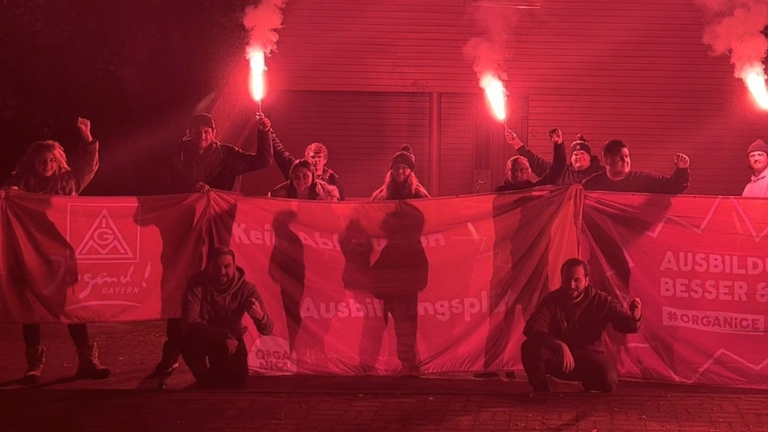 Das Bild zeigt Aktive Jugendliche mit einem Banner mit der Aufschrift "Ausbildung - Besser & Mehr!" und gezündeten roten Bengalo-Fackeln.